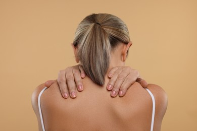 Photo of Mature woman suffering from pain in her neck on beige background, back view