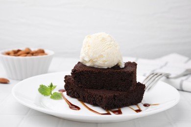 Photo of Tasty brownies served with ice cream and caramel sauce on white tiled table, closeup