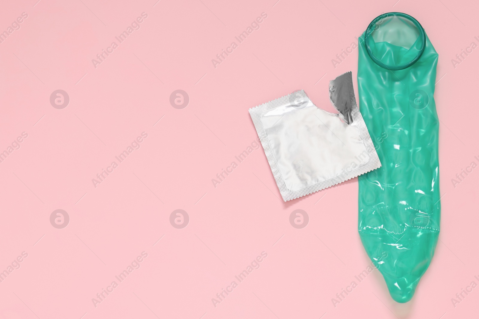 Photo of Unrolled condom and torn package on pink background, top view with space for text. Safe sex