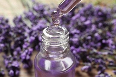 Natural oil dripping into bottle and lavender flowers on table, closeup. Cosmetic product