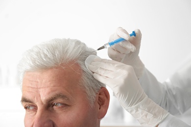 Senior man with hair loss problem receiving injection in salon, closeup