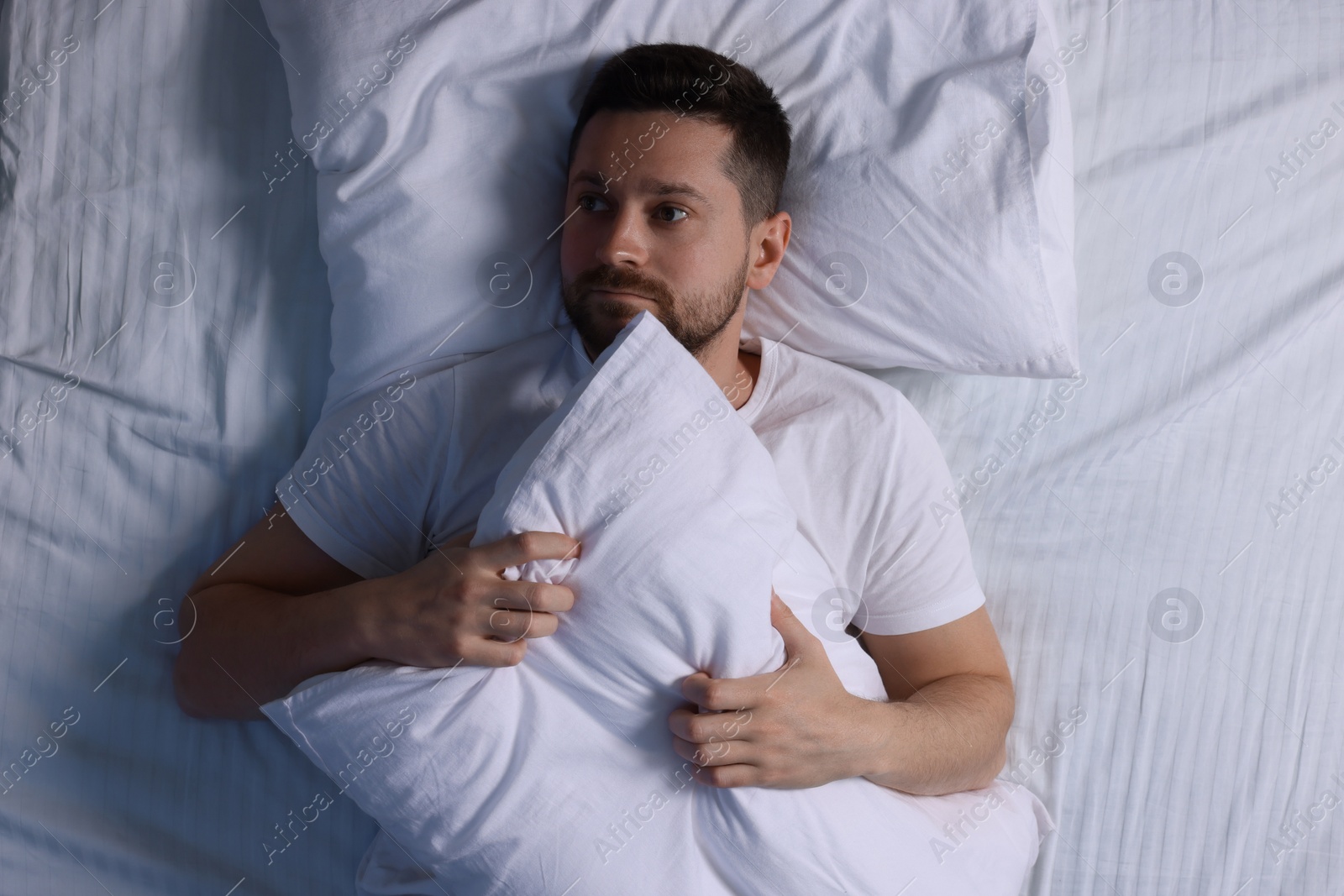 Photo of Sleepy man with pillow in bed, top view. Insomnia problem