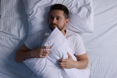 Photo of Sleepy man with pillow in bed, top view. Insomnia problem