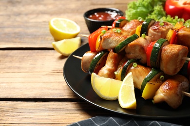 Photo of Delicious chicken shish kebabs with vegetables and lemon on wooden table, closeup. Space for text