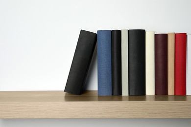 Photo of Many hardcover books on wooden shelf near white wall