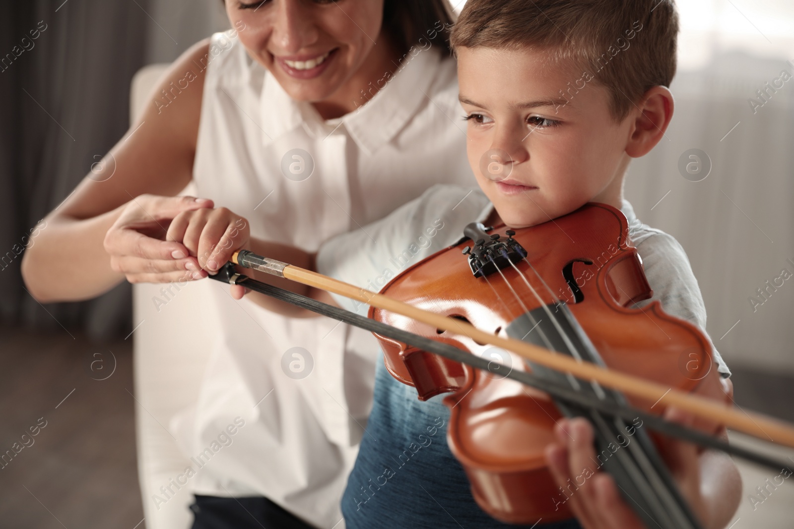 Photo of Young woman teaching little boy to play violin indoors, closeup