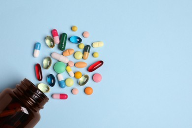 Plastic medical bottle with many different pills on light blue background, flat lay. Space for text