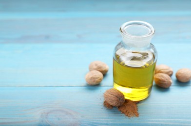 Photo of Bottle of nutmeg oil and nuts on turquoise wooden table, closeup. Space for text
