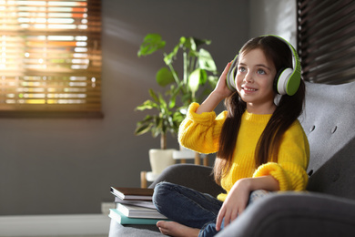 Photo of Cute little girl with headphones listening to audiobook at home