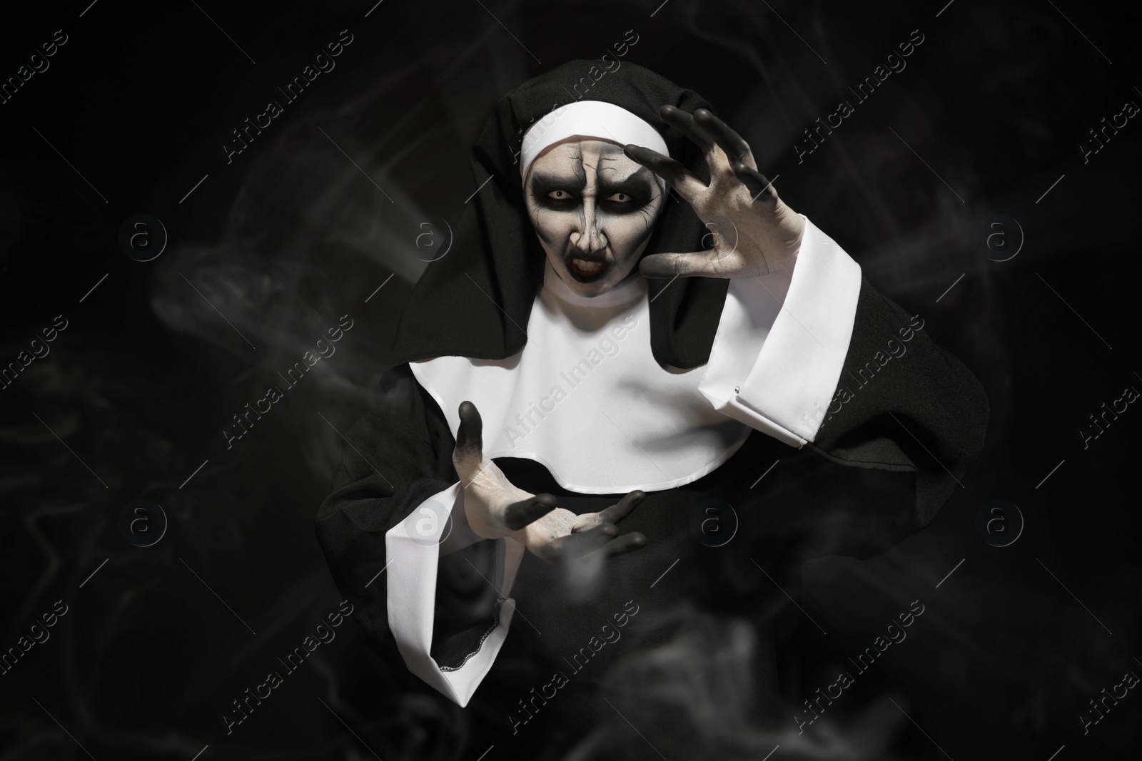 Photo of Portrait of scary devilish nun on black background. Halloween party look