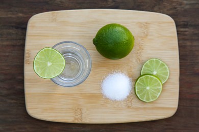 Photo of Mexican tequila shot with lime slices and salt on wooden table, top view. Drink made from agave