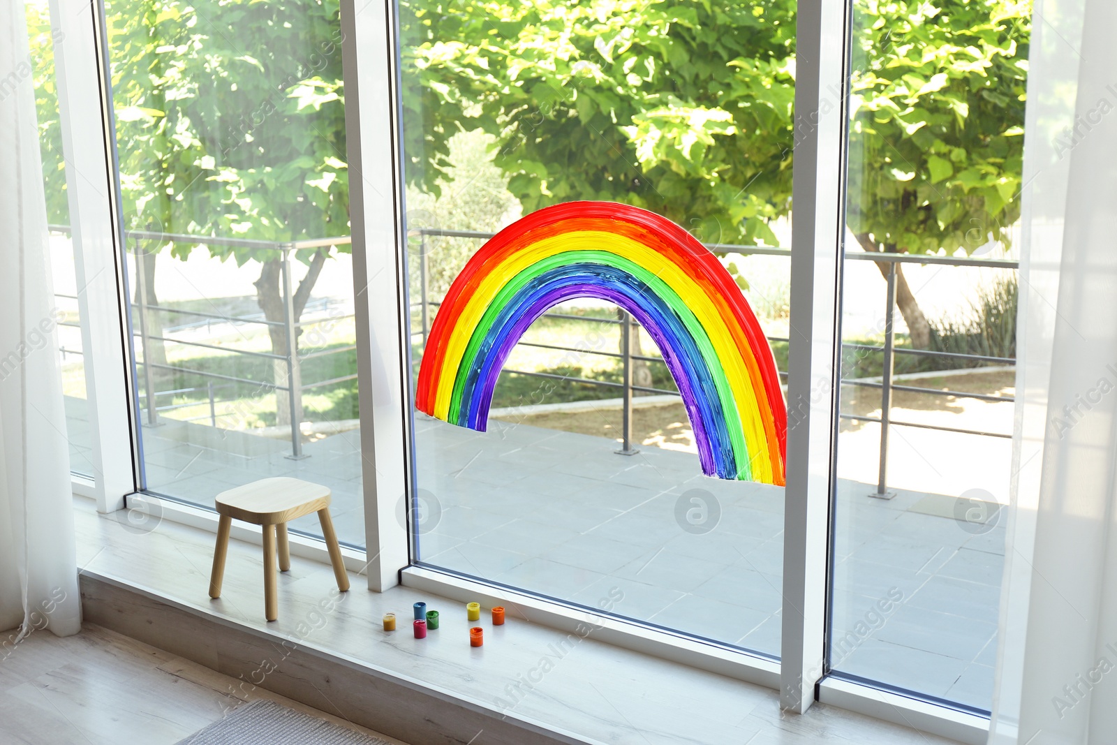 Photo of Painting of rainbow on window and paints indoors. Stay at home concept