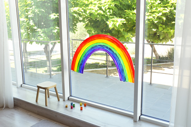 Photo of Painting of rainbow on window and paints indoors. Stay at home concept