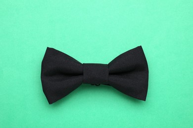 Stylish black bow tie on green background, top view