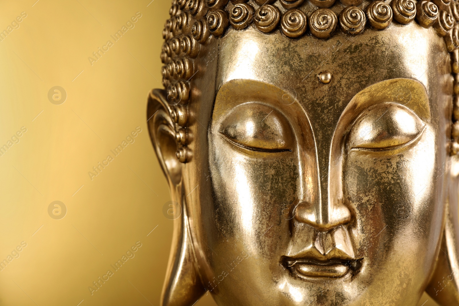 Photo of Buddha statue on golden background, closeup. Space for text