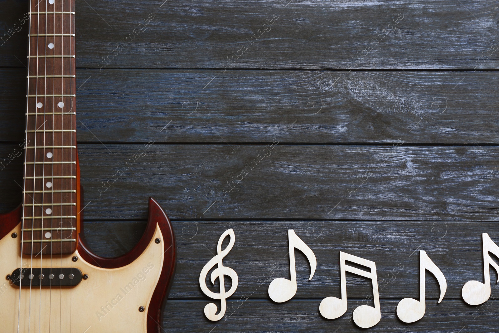 Photo of Music notes and guitar on wooden background, top view. Space for text