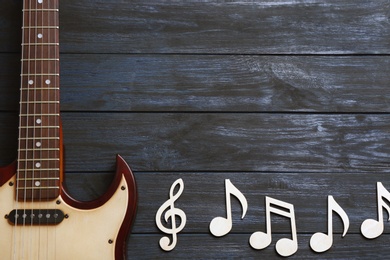 Photo of Music notes and guitar on wooden background, top view. Space for text