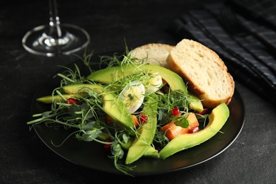 Photo of Salad with fresh organic microgreens in plate on black table, closeup