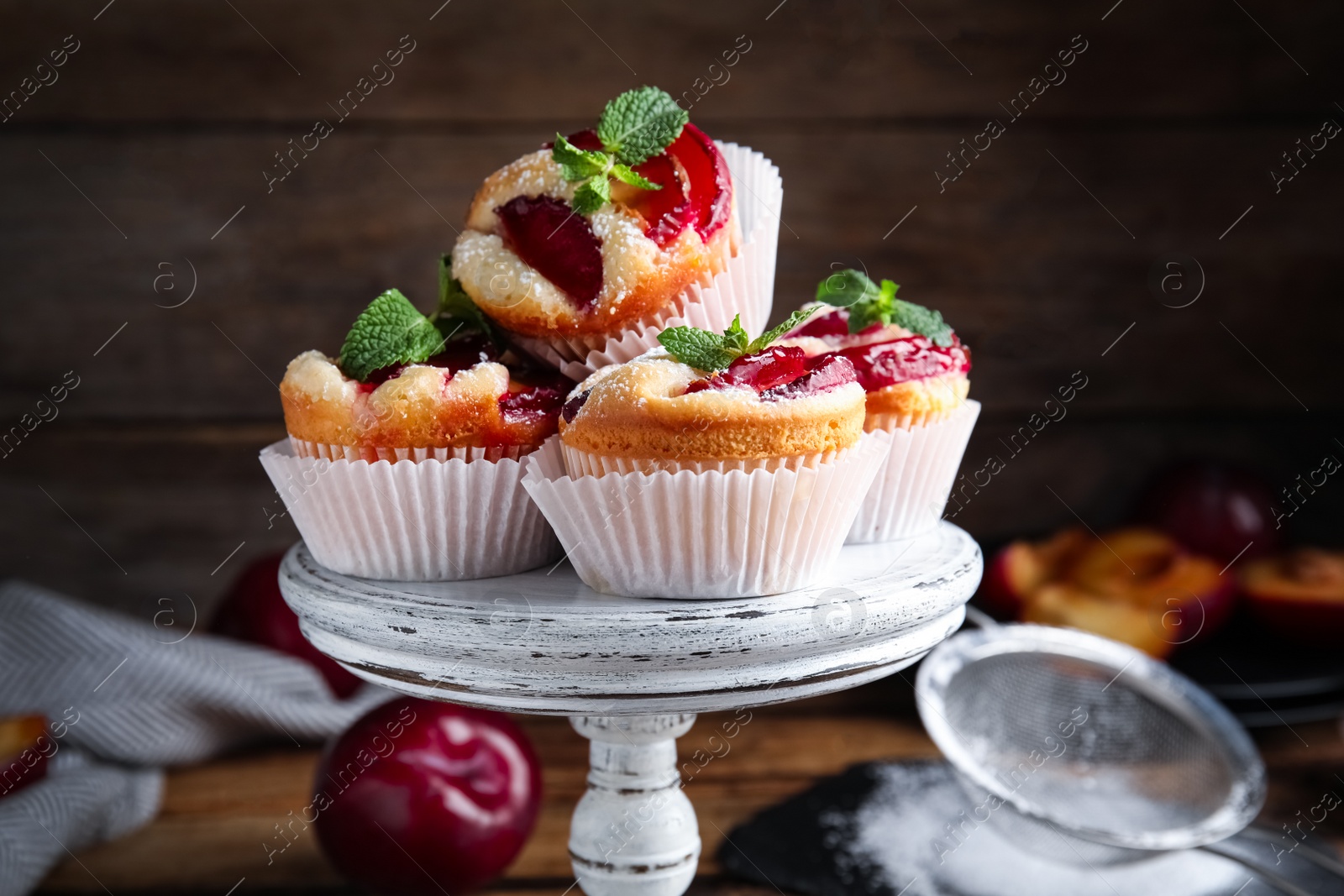 Photo of Delicious sweet cupcakes with plums on wooden stand, closeup