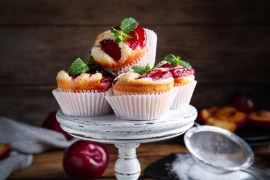 Delicious sweet cupcakes with plums on wooden stand, closeup