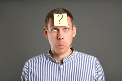 Emotional man with question mark on grey background