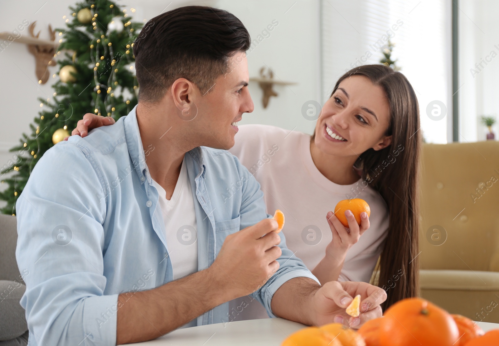 Photo of Happy couple with tangerines in room decorated for Christmas