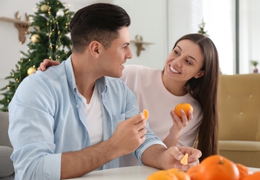 Happy couple with tangerines in room decorated for Christmas