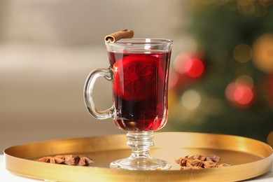 Delicious mulled wine in glass cup and anise stars on white table against blurred background