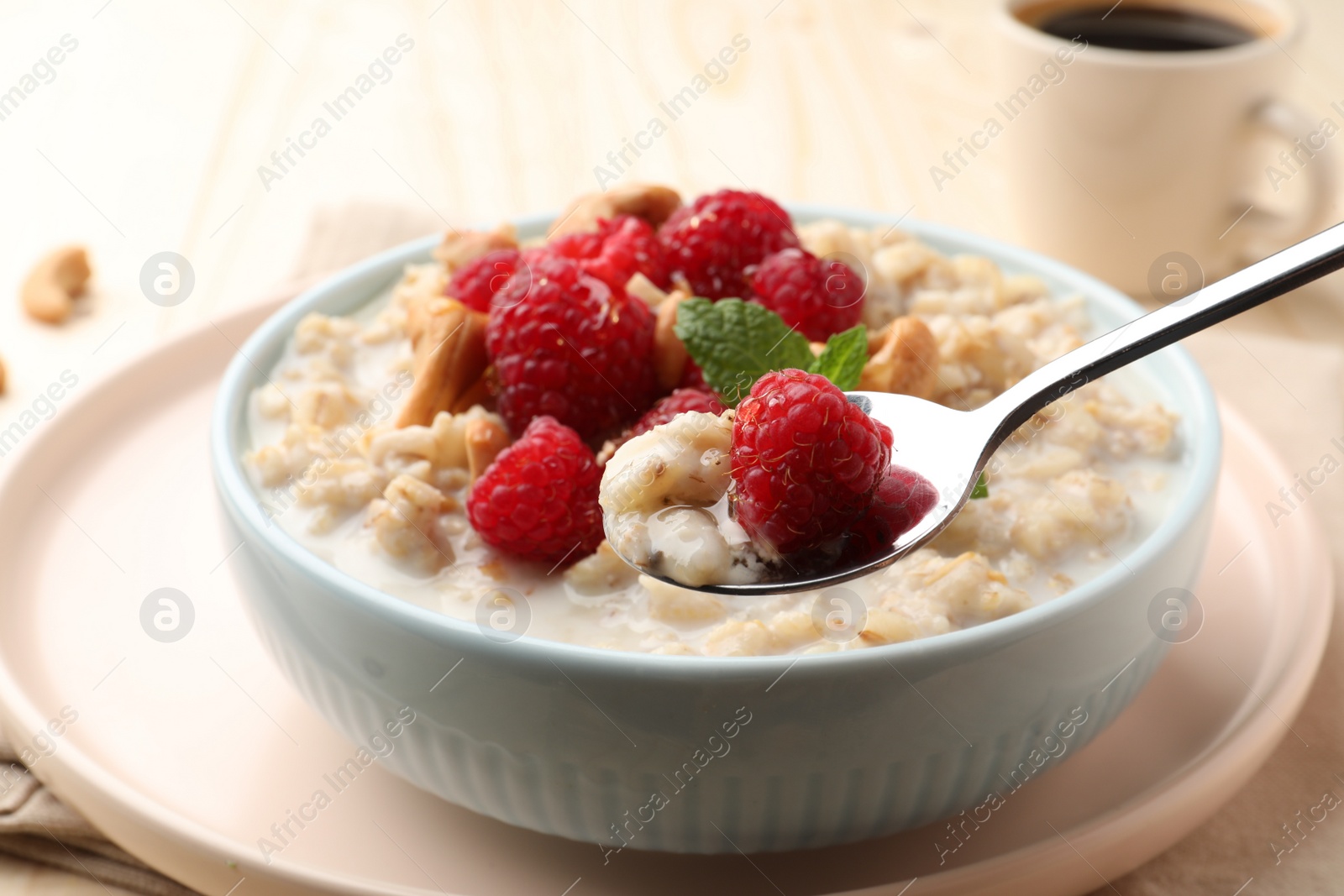 Photo of Bowl with tasty oatmeal porridge with nuts and raspberries on table, closeup. Healthy meal