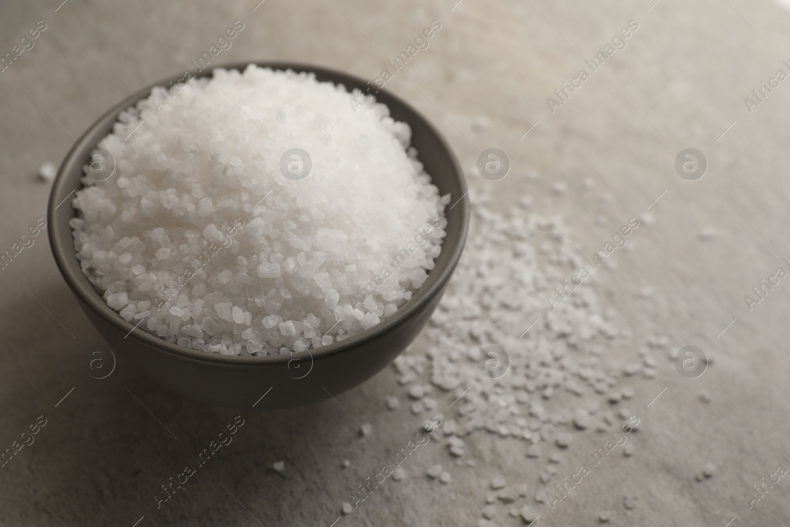 Photo of Natural salt in bowl on grey table, space for text