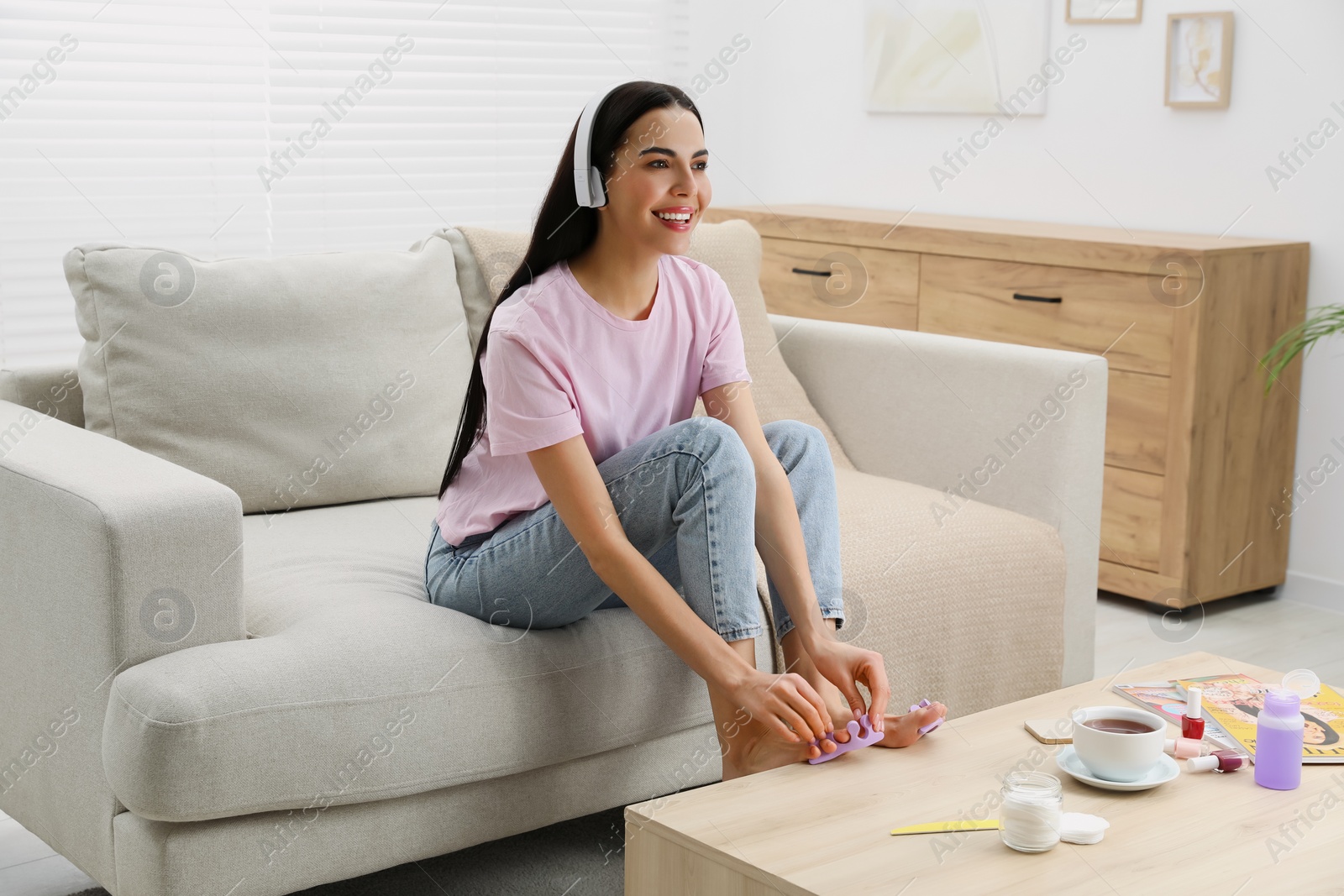 Photo of Beautiful young woman listening to music while preparing toenails for pedicure in living room