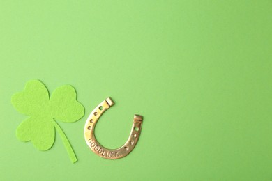 Photo of St. Patrick's day. Golden horseshoe and decorative clover leaf on green background, flat lay. Space for text