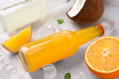 Photo of Tasty kombucha in glass bottles, fresh fruits and ice on white table, closeup