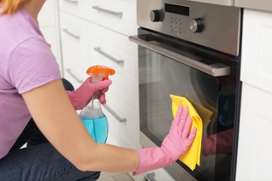 Woman cleaning oven with rag and detergent in kitchen, closeup