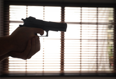 Man holding gun indoors, closeup. Space for text