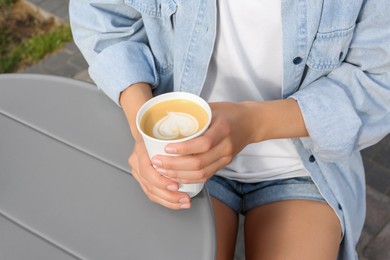 Coffee to go. Woman with paper cup of drink at grey table outdoors, closeup