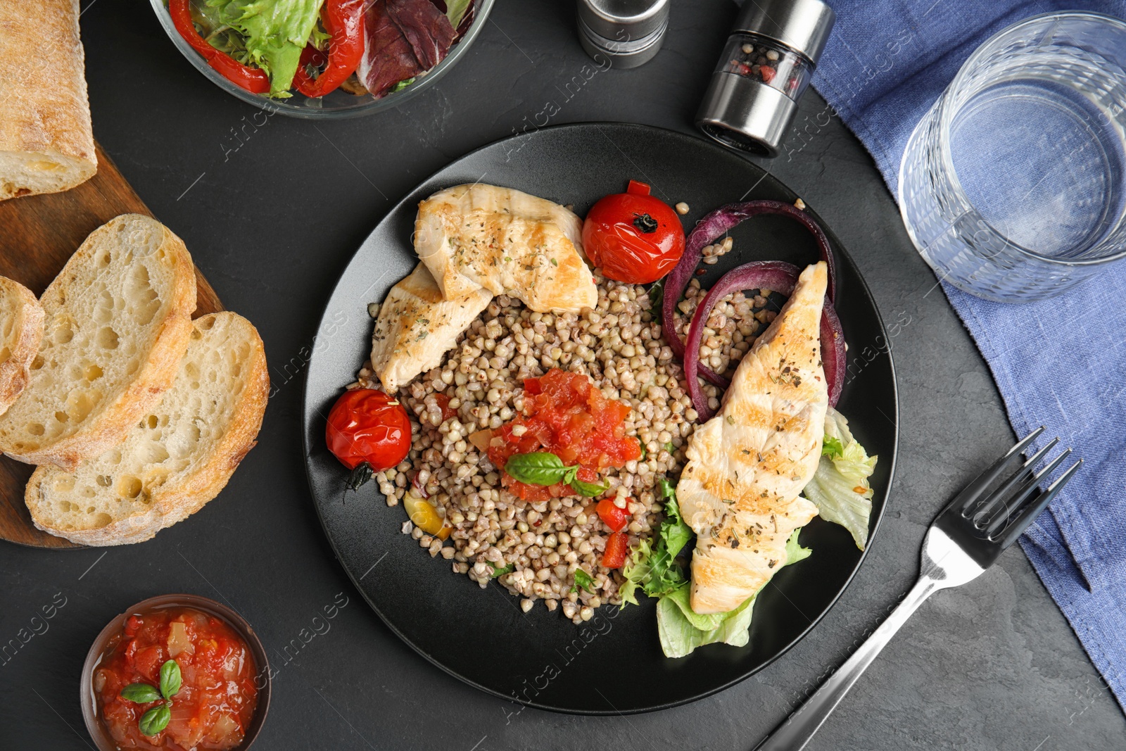 Photo of Tasty buckwheat porridge with meat and vegetables on black table, flat lay