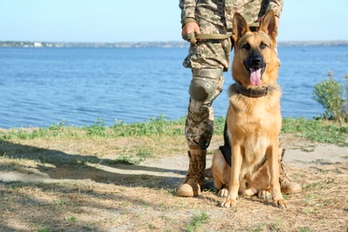Photo of Man in military uniform with German shepherd dog near river, closeup view