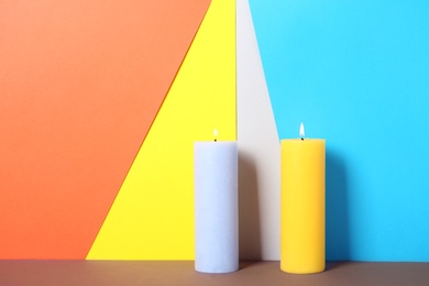 Decorative candles on table against color background