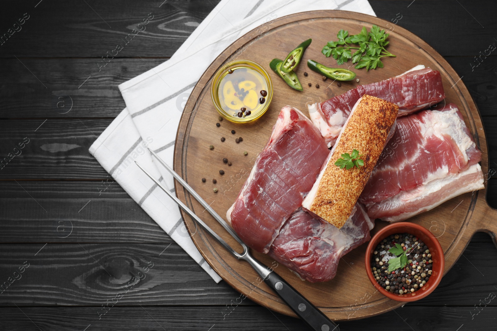 Photo of Pieces of raw pork belly, chili pepper, peppercorns, oil and parsley on black wooden table, top view. Space for text