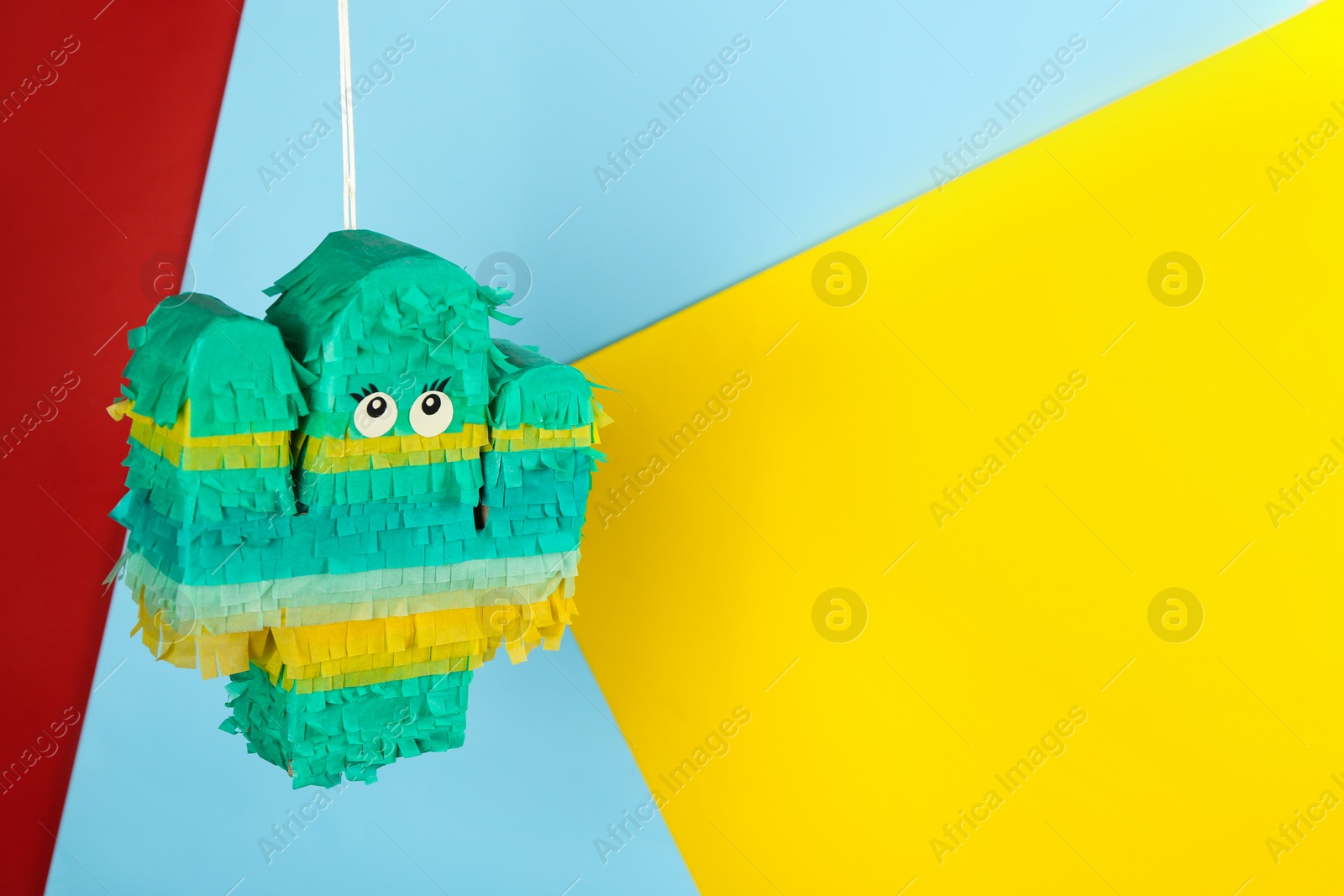 Photo of Cactus shaped pinata hanging on color background. Space for text