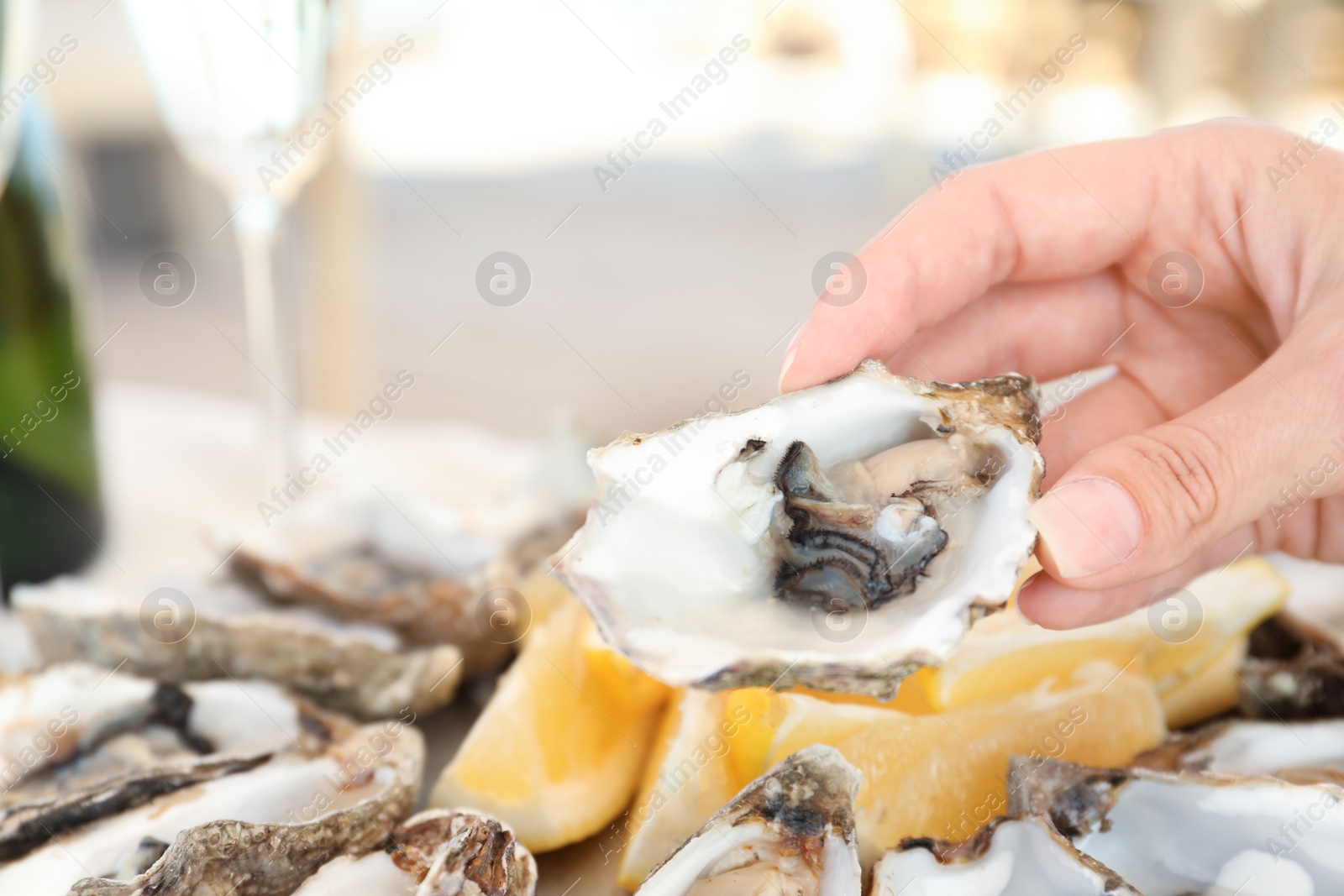 Photo of Woman holding fresh oyster over plate, focus on hand