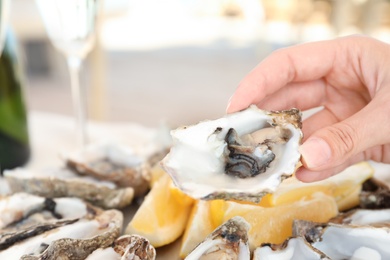 Woman holding fresh oyster over plate, focus on hand