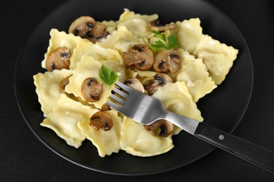 Photo of Delicious ravioli with mushrooms and fork on black table, closeup