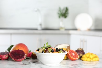 Photo of Delicious exotic fruit salad and ingredients on white marble table in kitchen