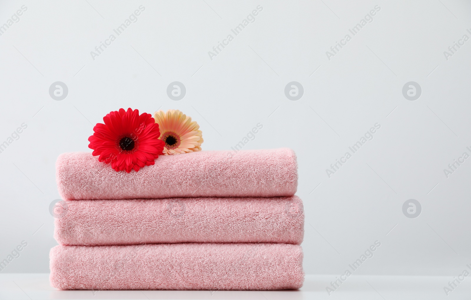 Photo of Stack of fresh towels with flowers on table against white background. Space for text