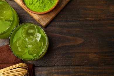 Photo of Delicious iced green matcha tea, powder and bamboo whisk on wooden table, flat lay. Space for text