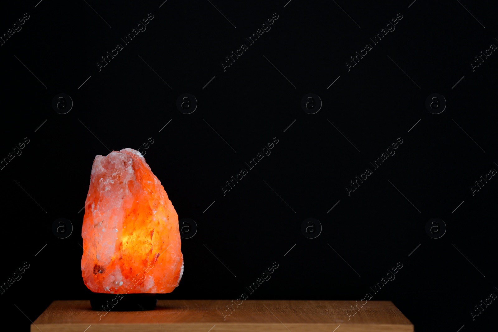 Photo of Himalayan salt lamp on table against black background. Space for text