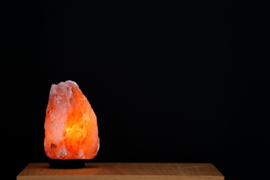 Photo of Himalayan salt lamp on table against black background. Space for text