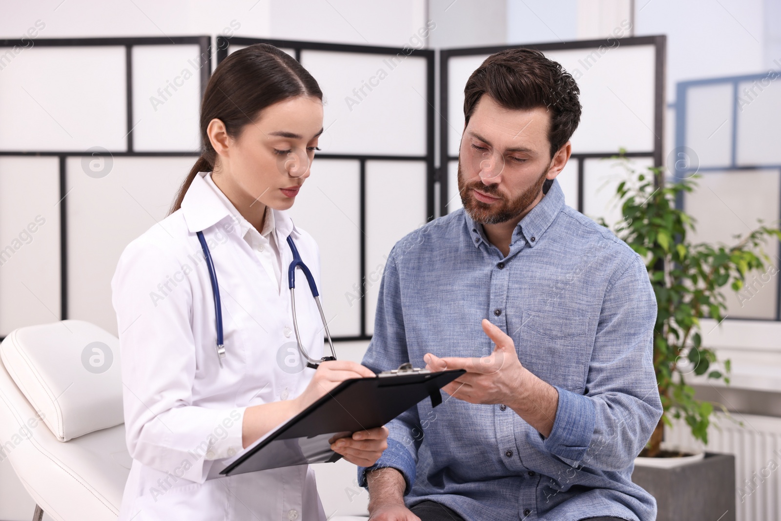 Photo of Doctor with clipboard consulting patient during appointment in clinic